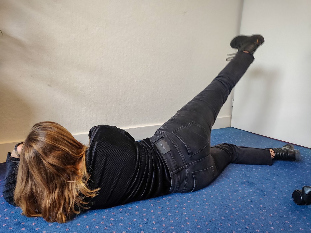 Medewerker doet de oefening genaamd Jane Fonda. Ze ligt op haar zij en tilt het bovenste been gestrekt omhoog.